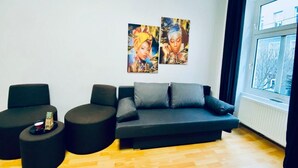 Una sala de estar moderna con un sofá negro, dos sillones negros, una mesita y dos obras de arte en la pared.