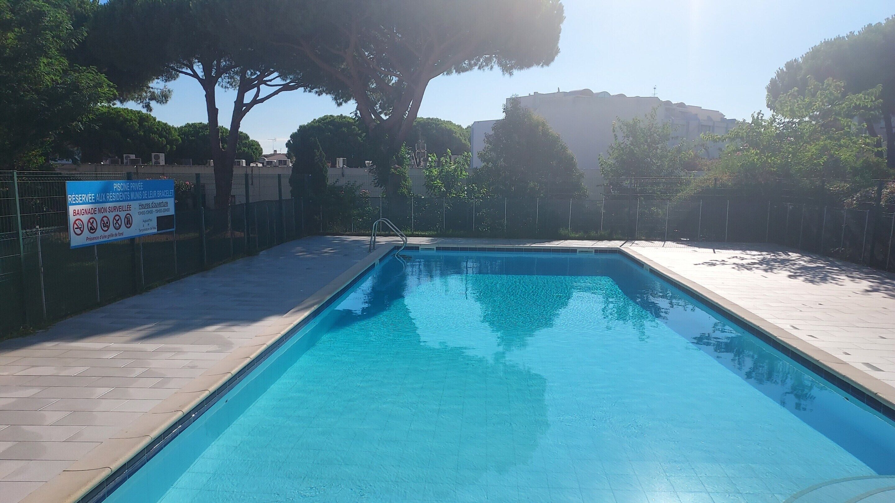 Ein rechteckiger Pool mit einer gefliesten Kante, umgeben von einem eingezäunten Bereich. Auf dem Zaun ist ein Schild angebracht, das darauf hinweist, dass der Pool privat und nur für Bewohner reserviert ist.