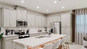 Een moderne keuken met witte kasten, roestvrijstalen apparatuur en een centraal kookeiland met barkrukken.