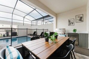 Un espace aménagé au bord de la piscine, avec une table en bois, des chaises et un coin barbecue.