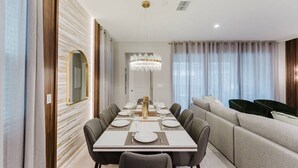 Een moderne eetruimte met een lange tafel gedekt voor zes personen, een kroonluchter en een bank op de achtergrond.