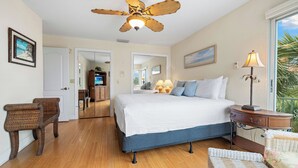 A bedroom with a large bed, a ceiling fan, a nightstand, a lamp, and a view of the outdoors. - Beautiful Townhouse 1/2 Block From Siesta key Village & The Beach! (Siesta Key)