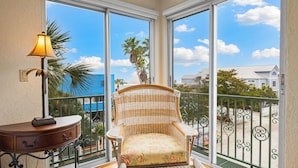 A balcony with a wicker chair, a small table with a lamp, and a view of the ocean and buildings. - Beautiful Townhouse 1/2 Block From Siesta key Village & The Beach! (Siesta Key)