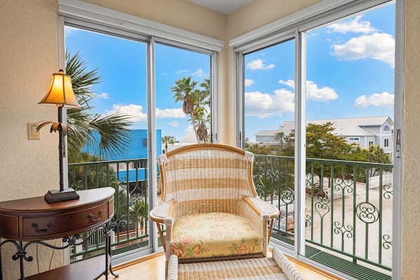 A balcony with a wicker chair, a small table with a lamp, and a view of the ocean and buildings. - Spanish villa half block from Siesta Key Beach & Village (Siesta Key)