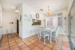 Un coin repas avec une table et des chaises blanches, un lustre et une horloge au mur.