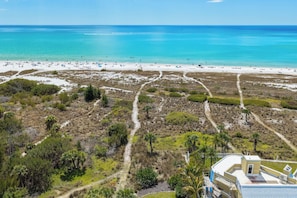 Vue aérienne d’une plage aux eaux turquoise et limpides, bordée d’un rivage sablonneux et d’une végétation clairsemée.