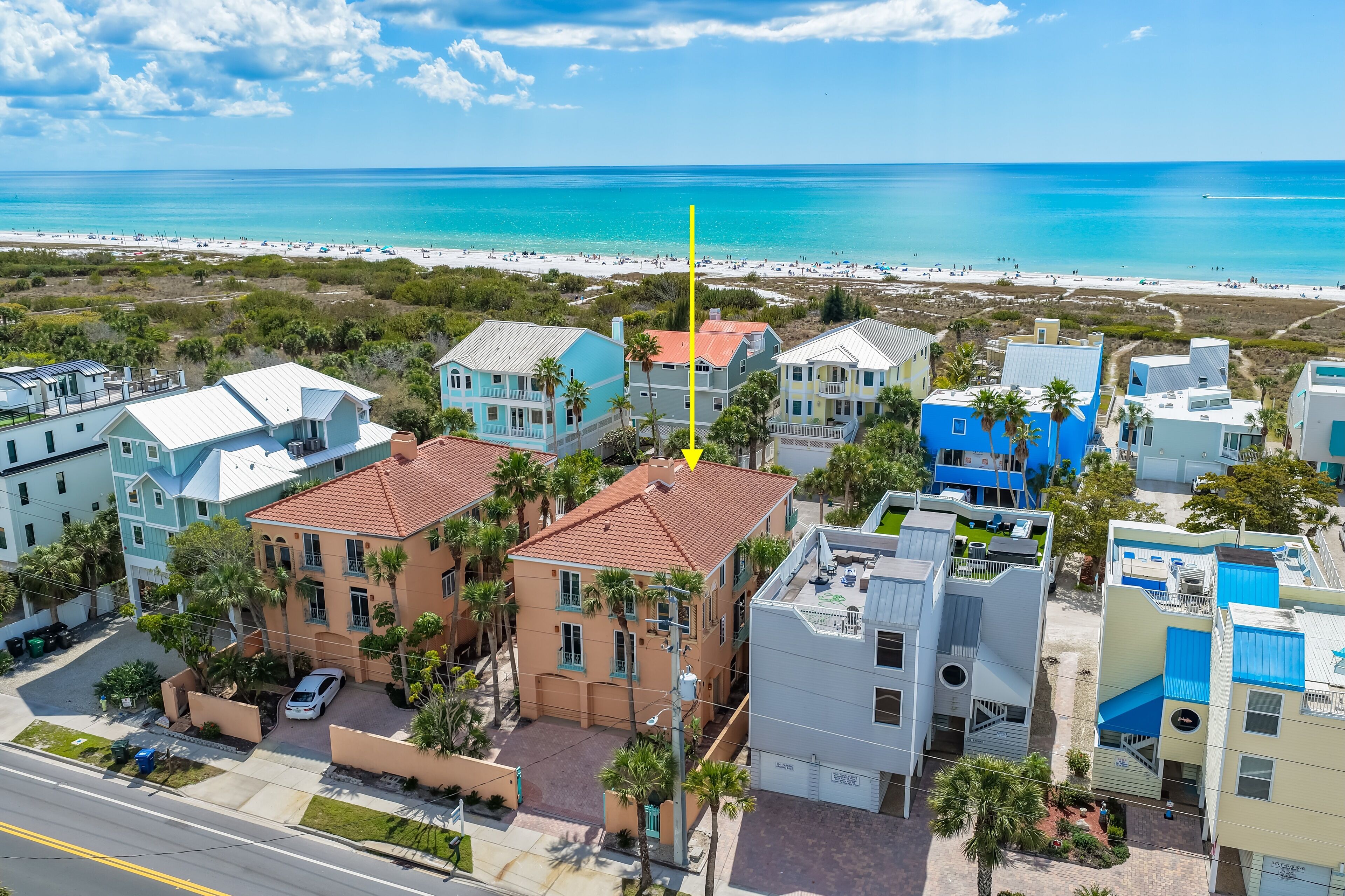 A coastal residential area with beachfront properties, including houses with red roofs and blue exteriors, and a view of the beach and ocean.