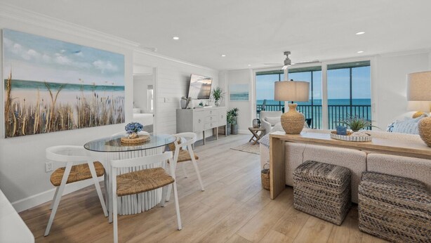 A modern kitchen with white cabinetry, a dining area with a glass table, and a view of the ocean through large windows. - Stunning Condo at Crystal Sands on Siesta Key! (Siesta Key)