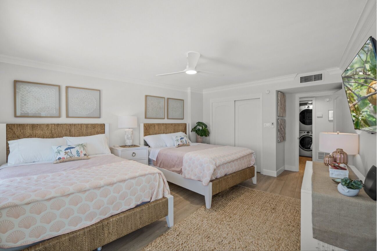 Un dormitorio con dos camas, ventilador de techo, lavadora y un amplio ventanal.