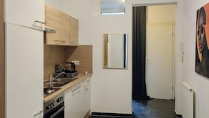 A compact kitchen with a stove, oven, and sink, a small window, and a door leading to another room. - Comfortable Room by Währinger Park, Shared Apt (Vienna)