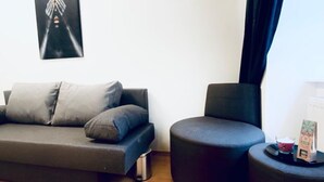 A modern living room with a sofa, a round chair, a small table with a candle and a box, and a trash bin. - Comfortable Room by Währinger Park, Shared Apt (Vienna)