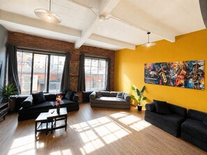 A modern living room with large windows, a black sofa, a grey sectional, and a vibrant abstract painting. - Central Apt Sleeps 8 | Bars, Restaurants & Parking (Liverpool)
