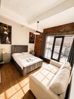 A modern bedroom with a large bed, a sofa, a nightstand, and a window with a view. - Central Apt Sleeps 8 | Bars, Restaurants & Parking (Liverpool)