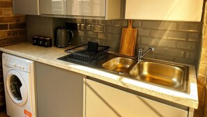 A compact kitchen with a washing machine, a sink, and a countertop with a drying rack.