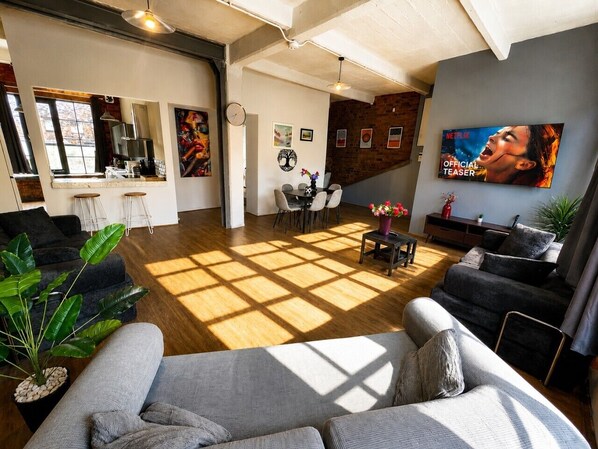 A spacious living area with a large window, a dining table, and a TV screen displaying an image. - Central Apt Sleeps 8 | Bars, Restaurants & Parking (Liverpool)