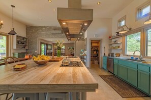Een moderne keuken met een centraal eiland, inbouwapparatuur en een groot raam dat voor natuurlijk licht zorgt.