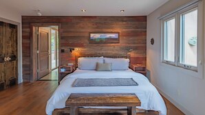 A bedroom with a wooden headboard, a bed with white linens, a bedside table, a nightstand, a window with blinds, and a door leading to another room. - 2 Culinary Suites in the heart of Wine Country! (Paso Robles)