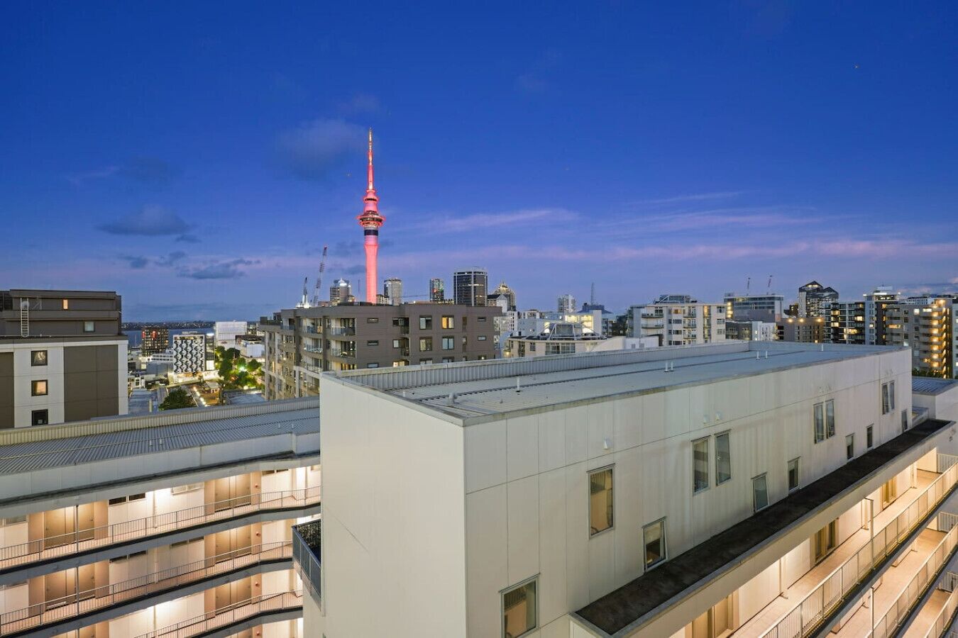 A modern building with multiple floors and balconies, featuring a prominent tower in the background.