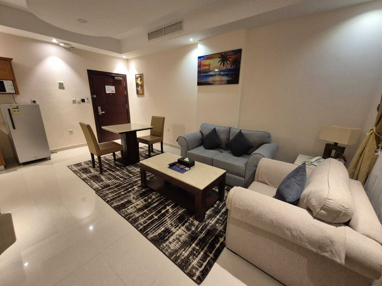 A living room with a sofa, a coffee table, a dining table with chairs, a refrigerator, and a painting on the wall.