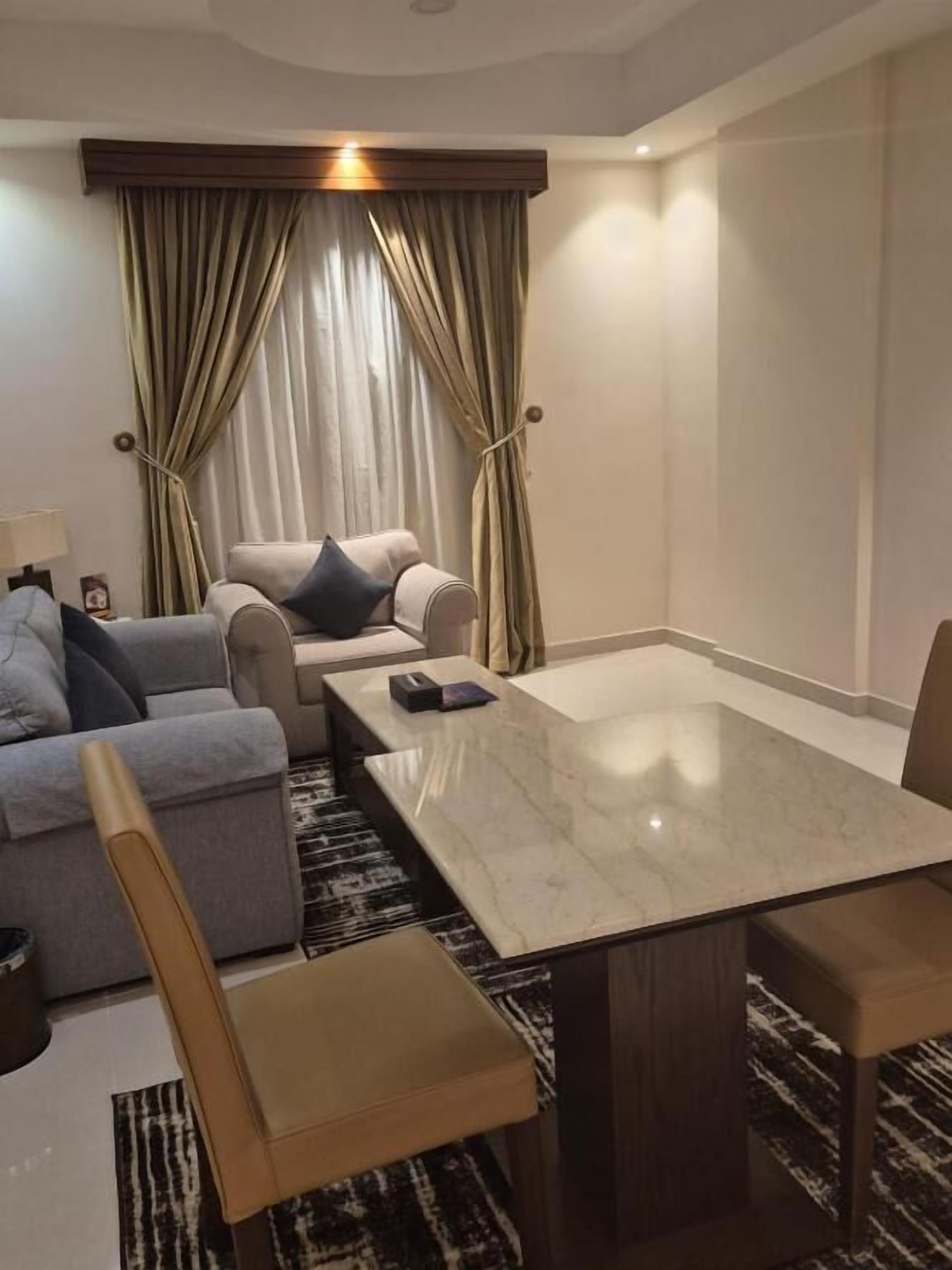 A modern hotel room with a marble dining table, a sofa, and a chair.