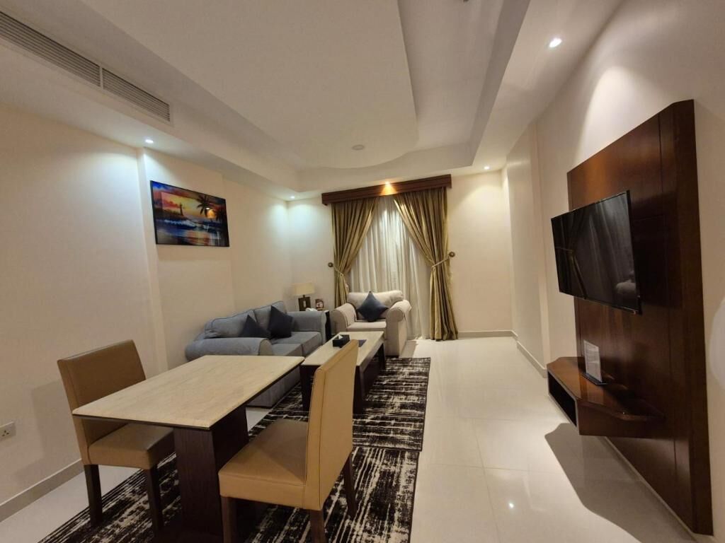 A modern living room with a sofa set, a dining table, and a flat-screen TV mounted on the wall.