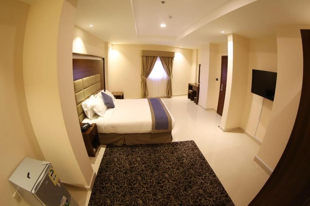 A hotel room with a bed, bedside tables, a TV, and a small refrigerator.