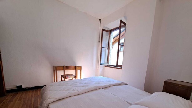 A small, clean room with a single bed, a wooden chair, and a window with wooden shutters. - GREEN DOLOMYTE Apartment (Schilpario)