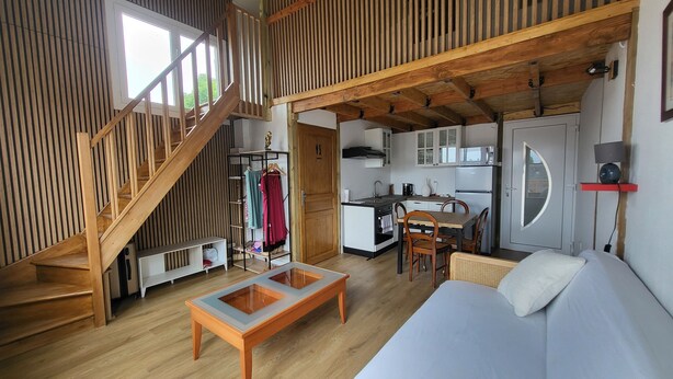 Um espaço de convívio compacto com escada de madeira, cozinha compacta, área de refeições e cama.
