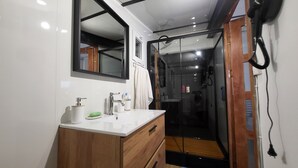 Uma casa de banho moderna com toucador de madeira, um espelho grande e cabine de duche em vidro.