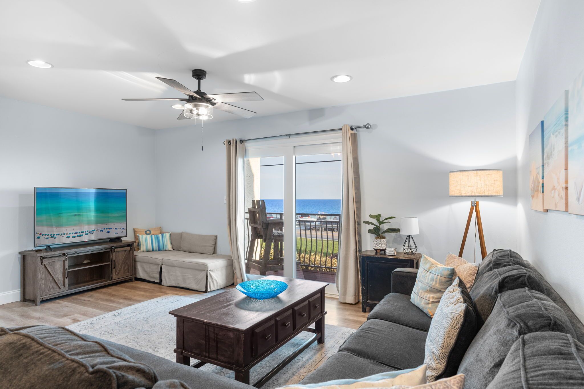 A living room with a television, sofa, coffee table, and a view of the ocean through a sliding glass door.