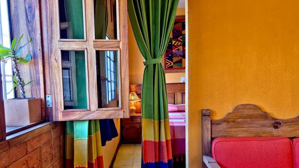 A narrow hallway with a wooden door, a window with a view, and a red sofa. - Sofia's Shawl (Oaxaca de Juárez)