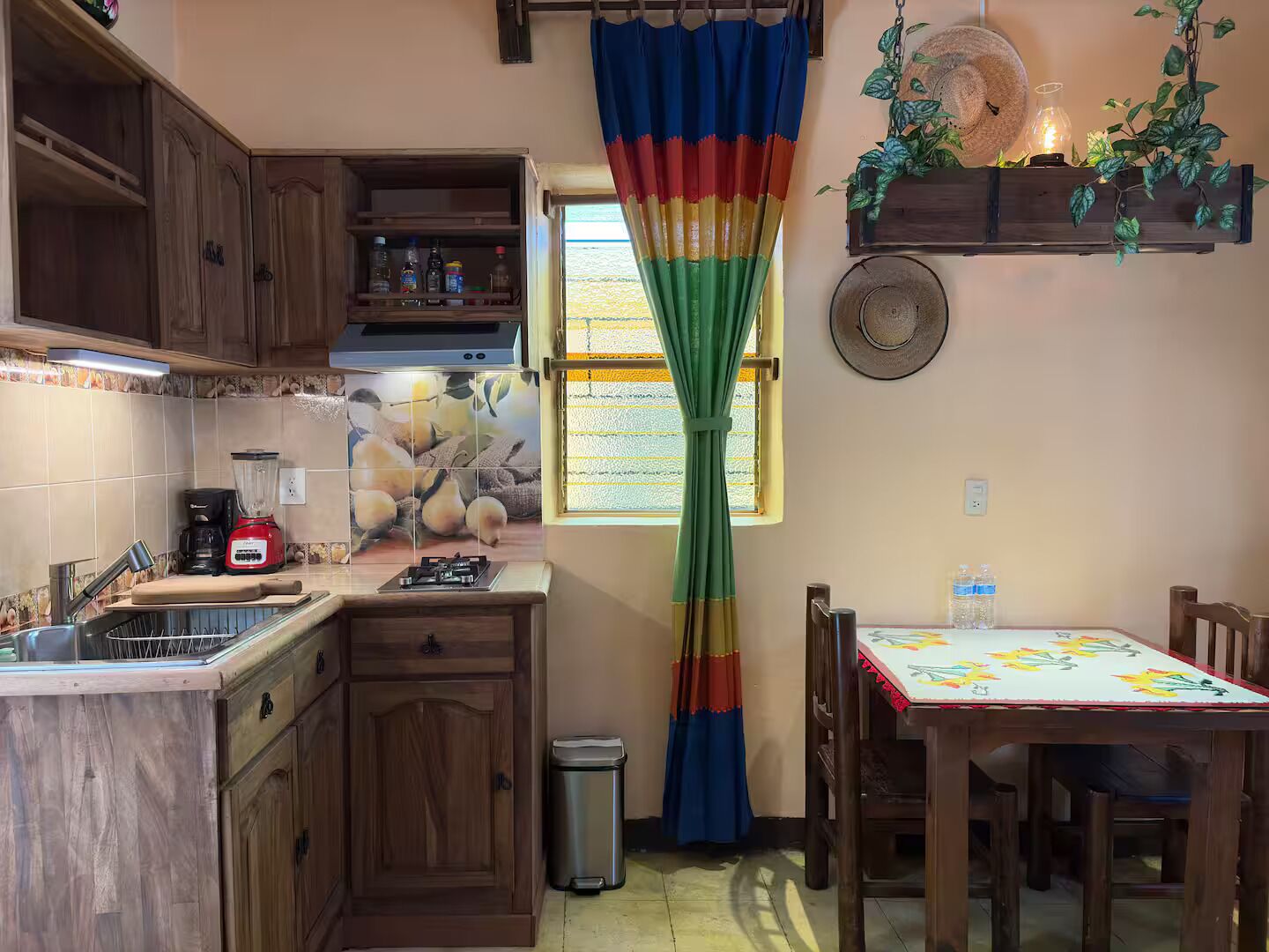 A kitchen with wooden cabinets, a gas stove, a sink, and a window with a colorful curtain.
