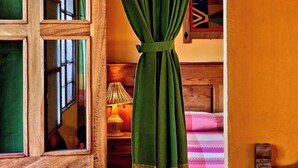 A room with a wooden window frame, a green curtain, a lamp, and a patterned bedspread. - Sofia's Shawl (Oaxaca de Juárez)