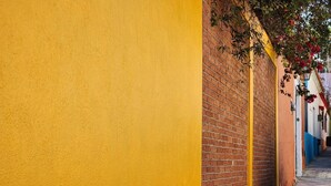 A narrow alleyway with yellow walls and a brick wall on one side. - Sofia's Shawl (Oaxaca de Juárez)
