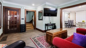 Een woonkamer met een houten salontafel, een rode bank, een aan de muur bevestigde televisie, en een eethoek met een witte tafel en stoelen.