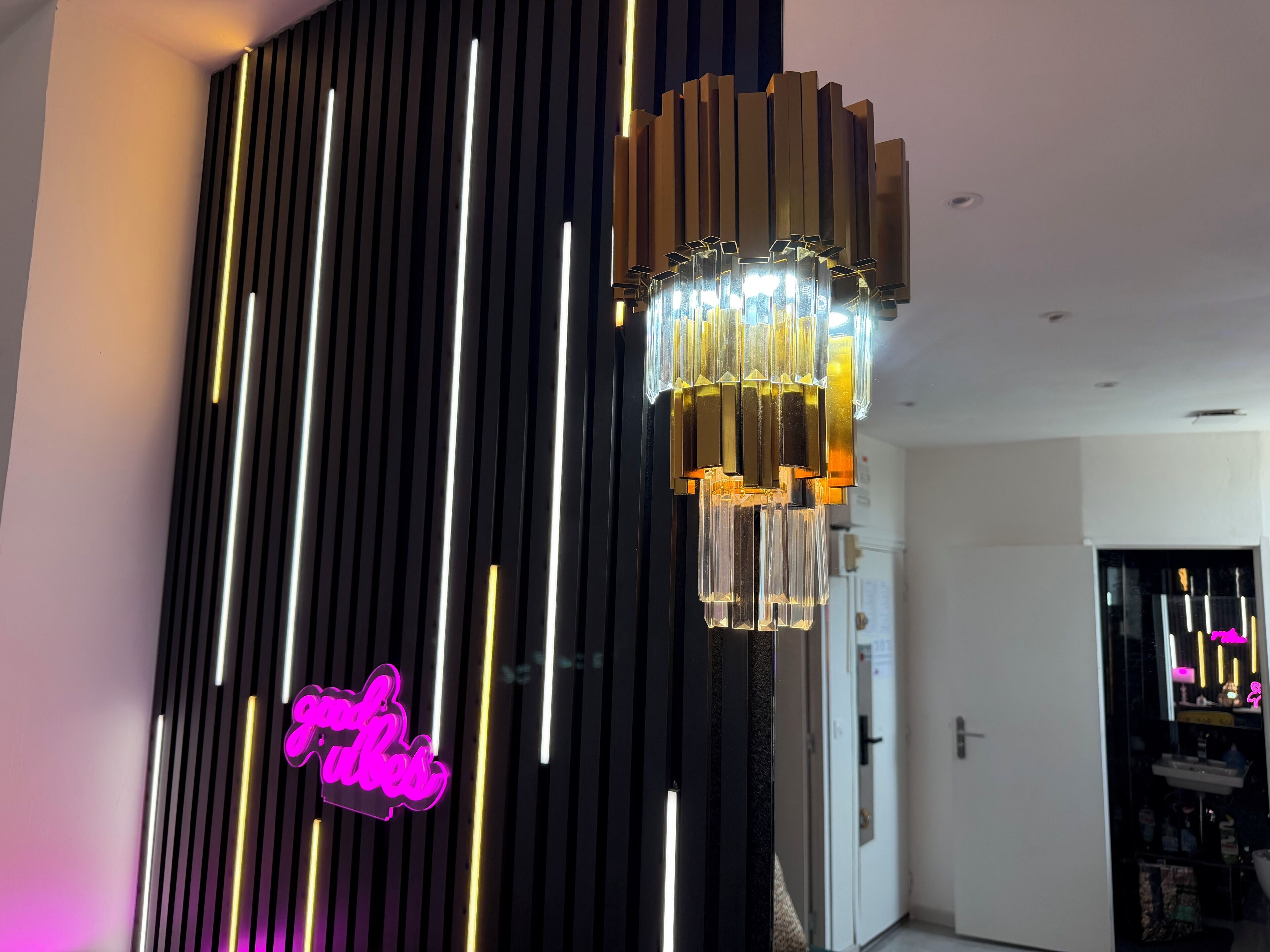 A modern interior with a vertical light strip design, a hanging chandelier, and a neon sign.