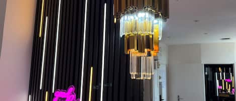 A modern interior with a vertical light strip design, a hanging chandelier, and a neon sign.