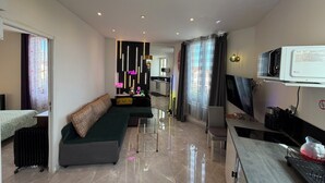 Habitación de hotel moderna con sofá, mesa de comedor, televisor y zona de cocina.