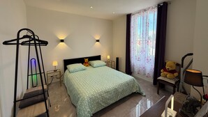 Habitación de hotel con cama, lámparas de noche, una silla colgante, un oso de peluche y una ventana con cortinas.