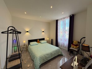 Ein Hotelzimmer mit einem Bett, Nachttischlampen, einem Hängestuhl, einem Teddybären und einem Fenster mit Vorhängen.