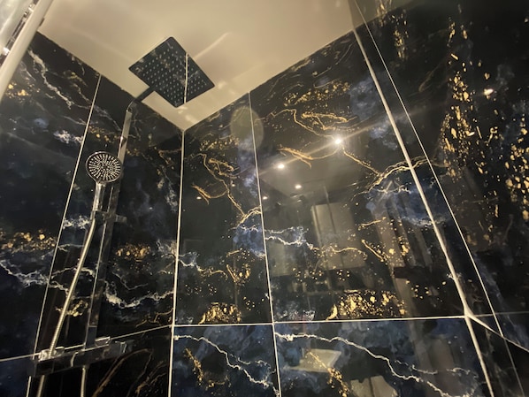 Ein modernes Badezimmer mit schwarzen Marmorfliesen und goldenen Akzenten, ausgestattet mit einer Duschkabine und einem Handbrausekopf.