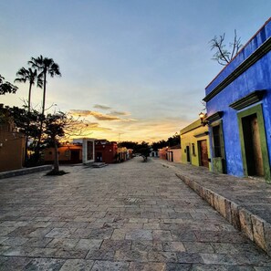 A cobblestone street lined with colorful buildings, palm trees, and a sunset in the background. - Spacious well located apartment (Oaxaca de Juárez)