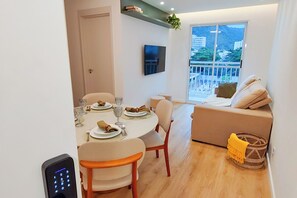 Un coin repas avec une table dressée pour quatre personnes, un canapé, un téléviseur fixé au mur et un balcon avec vue.