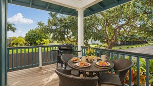 Eine überdachte Terrasse im Freien mit Korbmöbeln, einem Grill und einem Tisch, der mit Speisen und Getränken gedeckt ist.