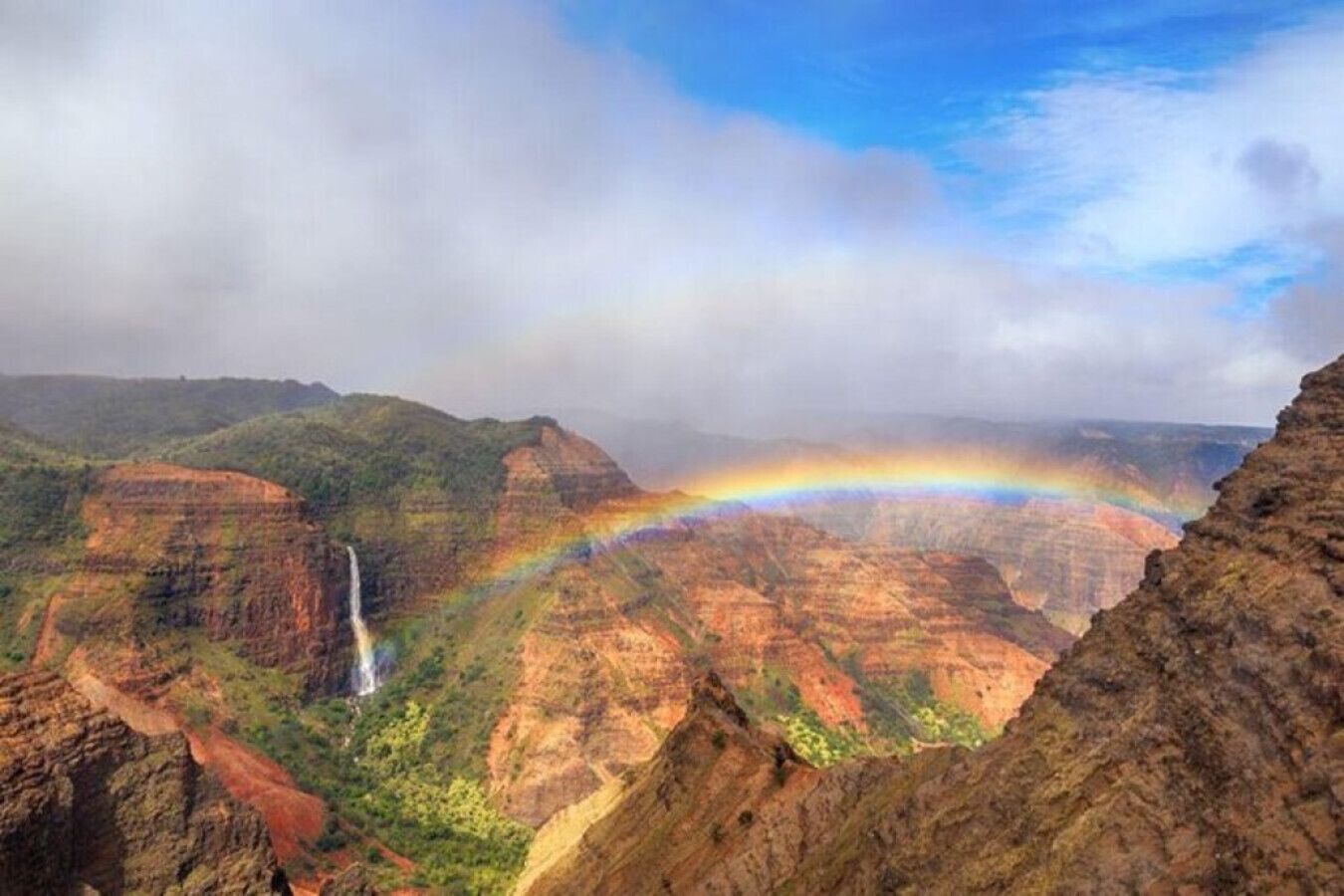 A canyon with a waterfall and a rainbow.