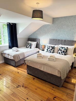 A modern hotel room with two beds, a large window with curtains, a grey textured wall, and a wooden floor. - No. 26 Killarney Holiday Village! (Killarney)