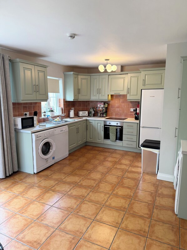 A kitchen with light green cabinets, a washing machine, a microwave, a toaster, and a refrigerator.