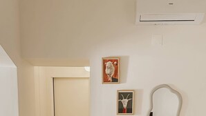 A living room with a beige sofa, a wooden side table, and a mirror. There is a door leading to another room and a staircase.