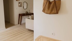 A room with a wooden floor, a white sofa, a wicker bench, and a hanging wicker bag.