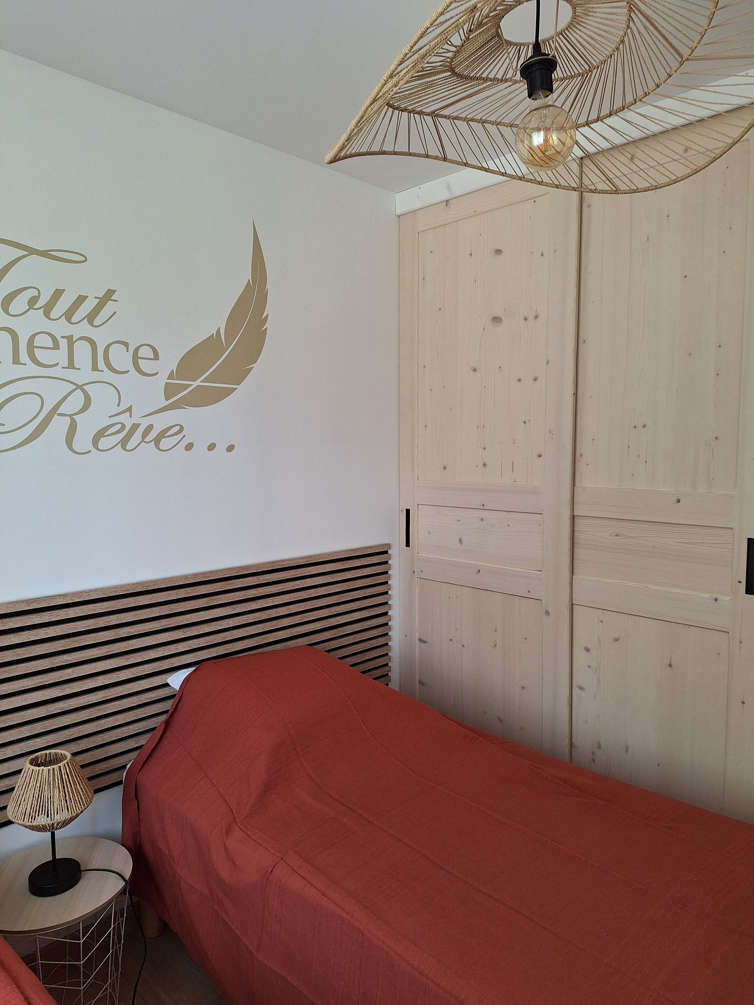 A bedroom with a bed, a wall-mounted lamp, a decorative wall with text, and a ceiling fan.